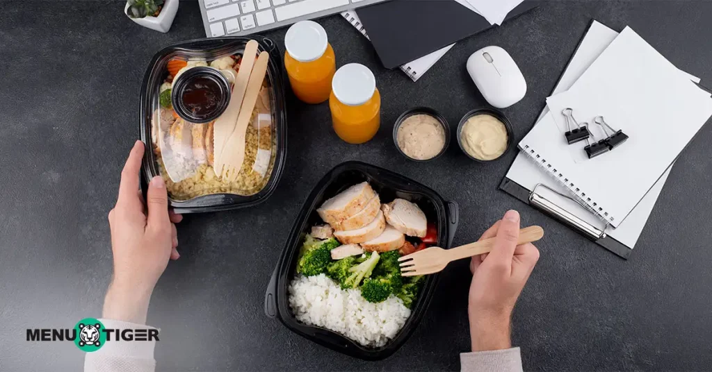 Person packing takeout meal boxes with rice, vegetables, and juice bottles on a table.